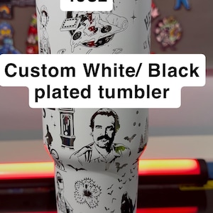 Könnte beinhalten: Ein weiß-schwarz beschichteter Becher mit einem Fassungsvermögen von 1,18 Litern. Der Becher ist mit schwarz-weißen Illustrationen verschiedener Charaktere und Objekte verziert. Der Text "Custom White/ Black plated tumbler" ist angezeigt.