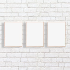 Puede incluir: Tres marcos de fotos vac&iacute;os con marcos de madera clara est&aacute;n colgados en una pared de ladrillo blanco.