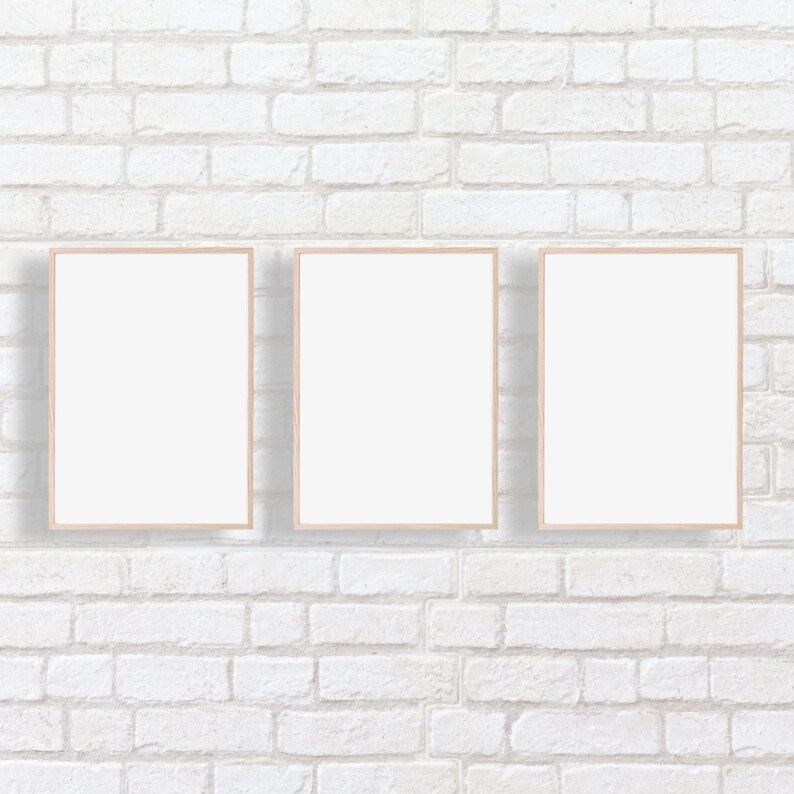 Puede incluir: Tres marcos de fotos vac&iacute;os con marcos de madera clara est&aacute;n colgados en una pared de ladrillo blanco.