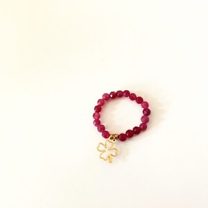 May include: A red beaded ring with a gold four-leaf clover charm.