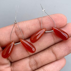 Puede incluir: Dos pares de cuentas de cornalina en forma de lágrima con bucles de alambre plateado. Las cuentas son de color rojo anaranjado intenso y están enhebradas en alambre plateado.
