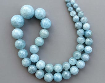 May include: A strand of polished, round, light blue aquamarine beads arranged in a curved shape. The beads vary in size, with the largest spheres positioned at one end and gradually decreasing in diameter toward the other end of the string.
