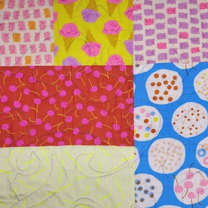 Pu&ograve; includere: Una colorata trapunta patchwork con vari motivi. La trapunta presenta quadrati con coni gelato, ciliegie e altri disegni giocosi in rosa, giallo, rosso e blu. La trapunta &egrave; cucita a macchina con un motivo ondulato.