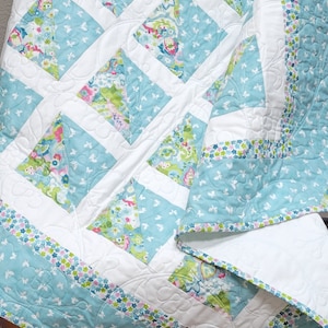 Könnte beinhalten: Eine blaue und weiße Steppdecke mit einem Blumenmuster und einem Schmetterlingsdesign. Die Steppdecke ist aus verschiedenen Stoffen gefertigt und hat eine weiße Rückseite.