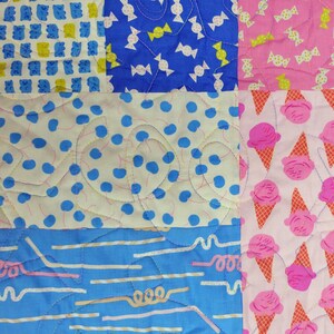 Pu&ograve; includere: Una colorata trapunta patchwork con vari motivi. La trapunta presenta quadrati con orsetti gommosi blu, caramelle bianche su blu, caramelle rosa, pois blu, coni gelato rosa e linee e vortici blu. La trapunta &egrave; trapuntata a macchina con filo giallo.