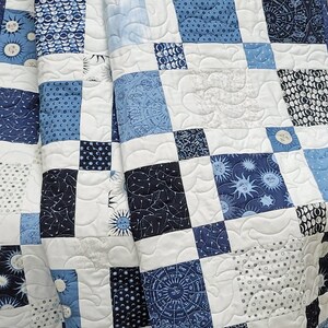 May include: A patchwork quilt featuring squares in shades of blue and white. The squares display celestial patterns like suns, moons, stars, and zodiac symbols. The quilt is quilted with a wavy pattern.