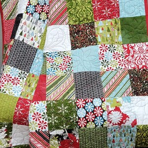 May include: A patchwork quilt with a Christmas theme. The quilt is made of various fabrics with different patterns, including snowflakes, candy canes, trees, and holly. The quilt is in shades of red, green, blue, white, and black.