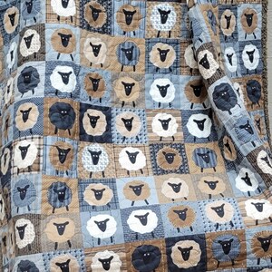 May include: A patchwork quilt featuring a repeating pattern of sheep in various colors. The sheep are set against a backdrop of blue, brown, and white squares. The quilt has a fringed edge.