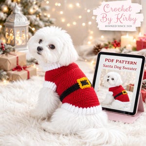May include: A white dog wearing a red and white crocheted Santa-style sweater with a black belt and gold buckle. A tablet displays a PDF pattern for the sweater. The image includes the text "Crochet By Kirby" and "Hooked Since 2020".