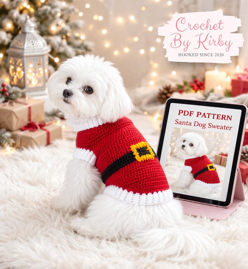 May include: A white dog wearing a red and white crocheted Santa-style sweater with a black belt and gold buckle. A tablet displays a PDF pattern for the sweater. The image includes the text "Crochet By Kirby" and "Hooked Since 2020".