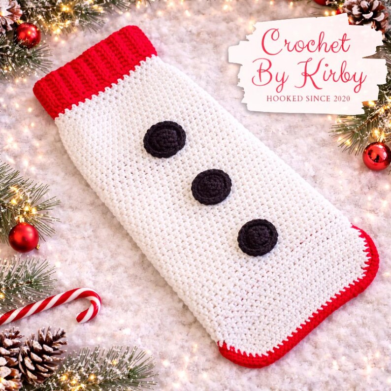 May include: A handmade crochet Christmas stocking in white with a red cuff and trim. Three black circular embellishments are sewn down the front. The stocking is decorated with Christmas ornaments and greenery.