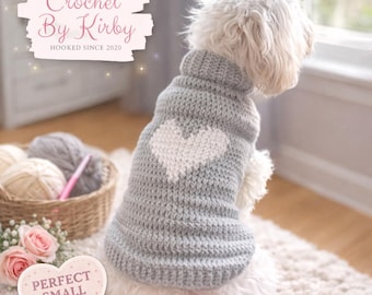 Puede incluir: Un suéter gris tejido a crochet para perros con un diseño de corazón blanco. El suéter, con cuello alto, lo lleva un perro blanco pequeño. La imagen incluye el texto "Crochet By Kirby" y "Hooked Since 2020".