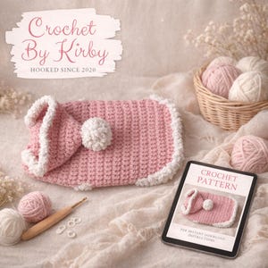 Könnte beinhalten: Ein rosa gehäkeltes Objekt mit weißer Bordüre und einem weißen Pompon. Das Bild zeigt auch ein Tablet mit einem Häkelmuster, Garn und dem Text "Crochet By Kirby, Hooked Since 2020".