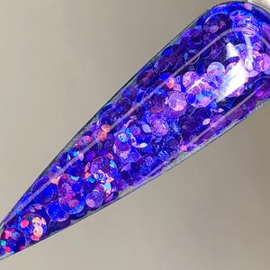 May include: A close-up of a clear nail polish bottle filled with iridescent blue and purple glitter.