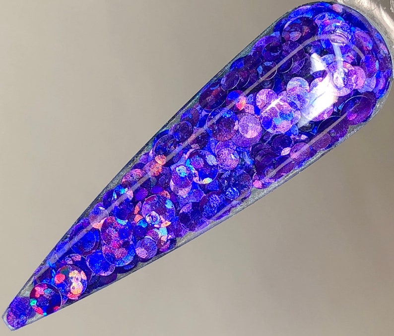 May include: A close-up of a clear nail polish bottle filled with iridescent blue and purple glitter.