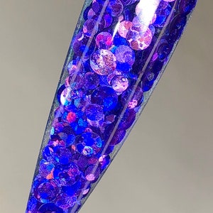 May include: A clear nail polish bottle filled with iridescent blue and purple glitter. The glitter is in a variety of sizes and shapes.