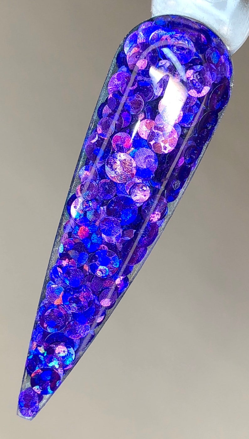 May include: A clear nail polish bottle filled with iridescent blue and purple glitter. The glitter is in a variety of sizes and shapes.