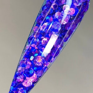May include: A close-up of a clear nail polish bottle filled with iridescent blue and purple glitter.