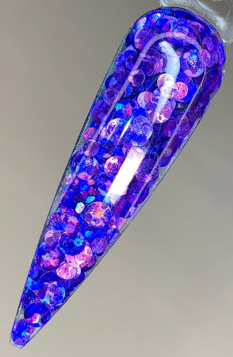 May include: A close-up of a clear nail polish bottle filled with iridescent blue and purple glitter.