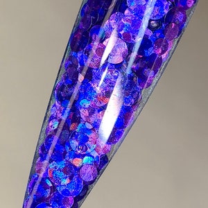 May include: A clear container filled with iridescent blue and purple glitter. The glitter is in the shape of small circles.