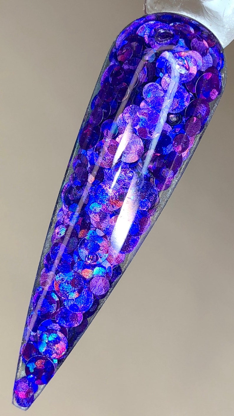 May include: A clear container filled with iridescent blue and purple glitter. The glitter is in the shape of small circles.