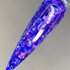 May include: A close-up of a nail with a clear base and a layer of iridescent blue and purple glitter.