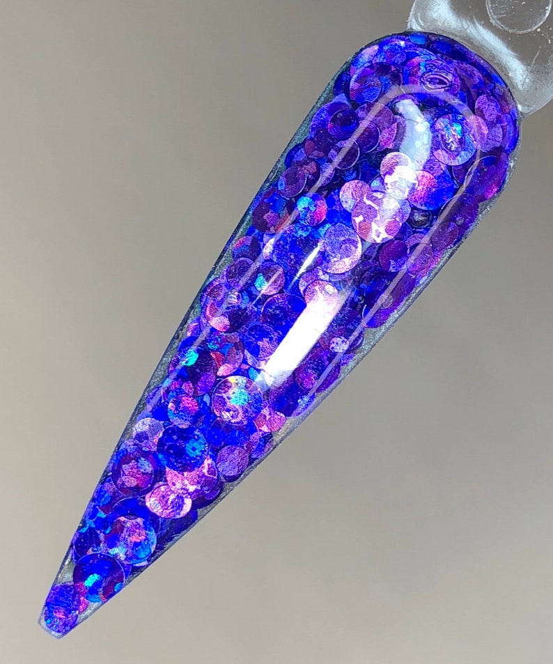May include: A close-up of a nail with a clear base and a layer of iridescent blue and purple glitter.