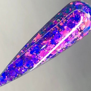 Könnte beinhalten: Eine durchsichtige Nagellackflasche gefüllt mit schimmerndem Glitzer in den Farben Rosa, Blau und Lila.