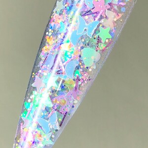 以下が含まれることがあります： 星、月、蝶、ハートなど、様々な形をした虹色のグリッターが詰まった透明なネイルポリッシュボトルです。