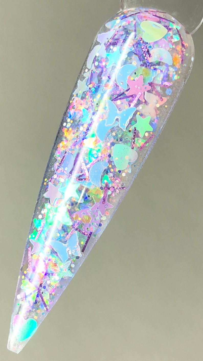 以下が含まれることがあります： 星、月、蝶、ハートなど、様々な形をした虹色のグリッターが詰まった透明なネイルポリッシュボトルです。