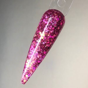 Könnte beinhalten: Nahaufnahme eines rosafarbenen Glitzer-Nagellacks. Der Lack ist auf einen langen, spitzen Nagel-Tipp aufgetragen.