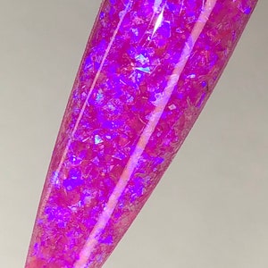 K&ouml;nnte beinhalten: Ein Nagelmuster mit einem lebendigen, irisierenden rosa- und lilafarbenen Glitzerdesign. Der Glitzer ist in einer klaren Basis eingebettet und erzeugt einen schimmernden Effekt. Der Nagel ist in einem langen, spitzen Stil geformt.