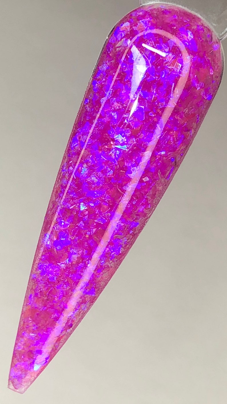 K&ouml;nnte beinhalten: Ein Nagelmuster mit einem lebendigen, irisierenden rosa- und lilafarbenen Glitzerdesign. Der Glitzer ist in einer klaren Basis eingebettet und erzeugt einen schimmernden Effekt. Der Nagel ist in einem langen, spitzen Stil geformt.