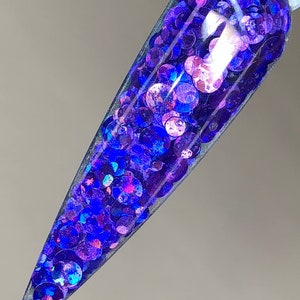May include: A clear nail polish bottle filled with iridescent blue and purple glitter. The glitter is in various sizes and shapes, creating a sparkly effect.