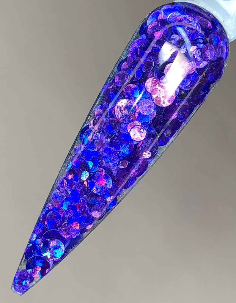 May include: A clear nail polish bottle filled with iridescent blue and purple glitter. The glitter is in various sizes and shapes, creating a sparkly effect.