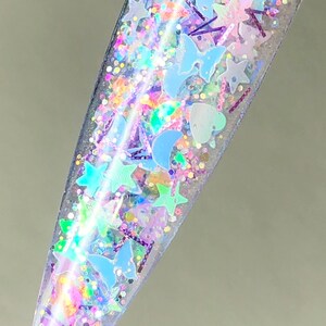 以下が含まれることがあります： 星、ハート、蝶など様々な形をした虹色のグリッターが詰まった透明なボトル。グリッターは薄い青、ピンク、紫のミックスです。