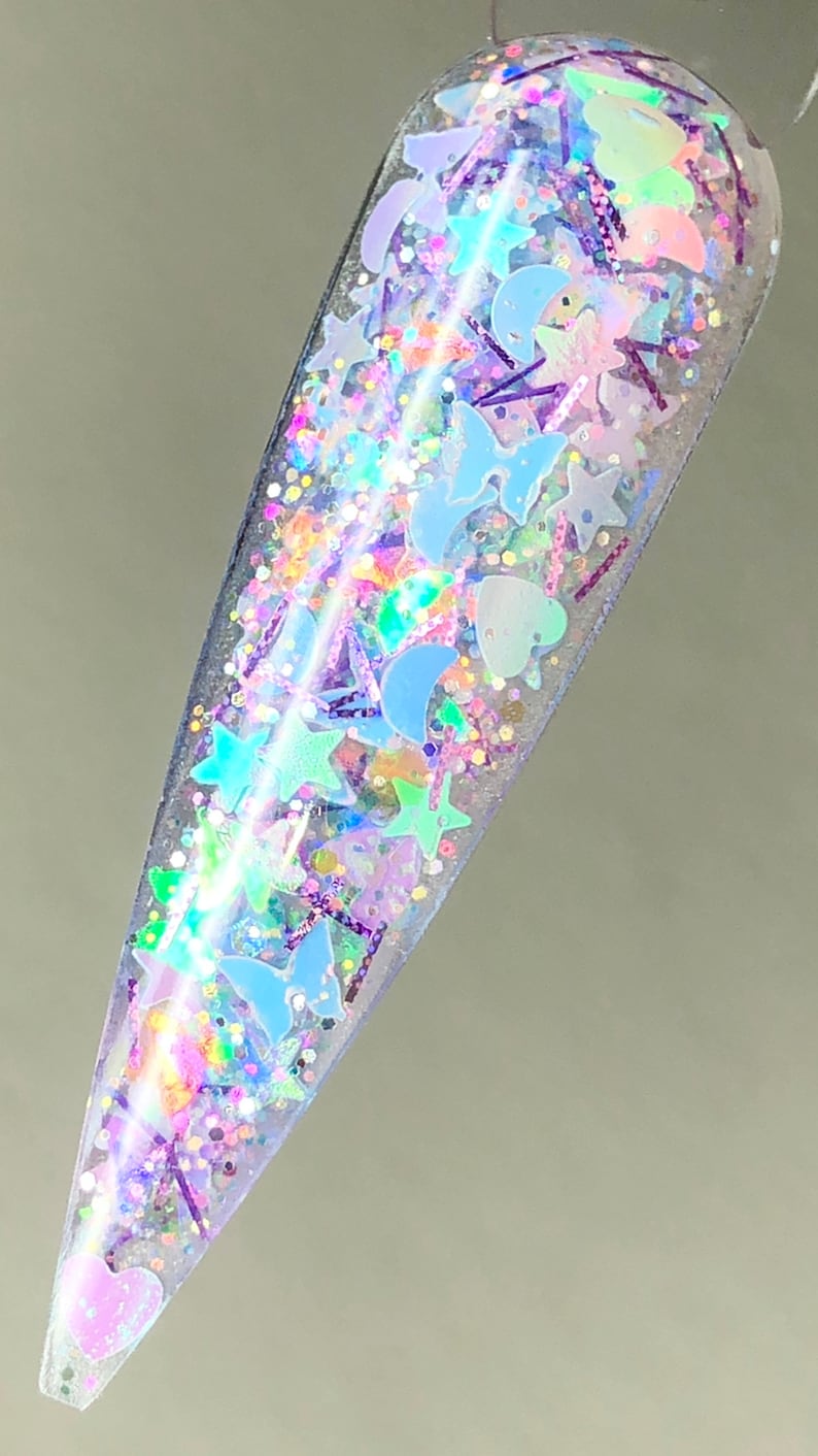 以下が含まれることがあります： 星、ハート、蝶など様々な形をした虹色のグリッターが詰まった透明なボトル。グリッターは薄い青、ピンク、紫のミックスです。