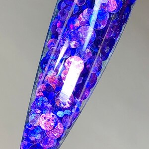May include: A clear container filled with iridescent blue and purple glitter. The glitter is in the shape of small circles.