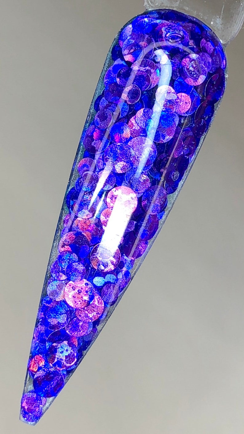May include: A clear container filled with iridescent blue and purple glitter. The glitter is in the shape of small circles.