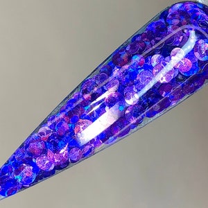 May include: A close-up of a clear nail tip with a layer of iridescent blue and purple glitter.