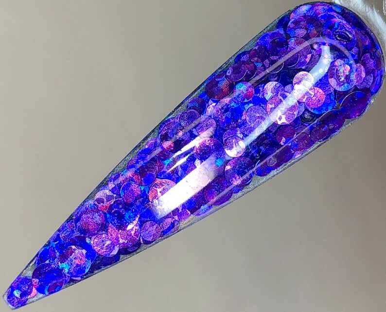 May include: A close-up of a clear nail tip with a layer of iridescent blue and purple glitter.
