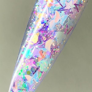 以下が含まれることがあります： 星、月、蝶など様々な形をした虹色のグリッターが詰まった透明なネイルポリッシュボトルです。