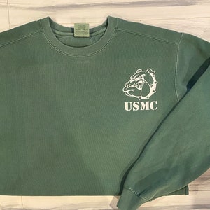 May include: A green sweatshirt with a white bulldog graphic and the text "USMC" on the front.