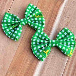 May include: Two green and white gingham hair bows with a yellow John Deere logo. The bows are tied in a bow shape.