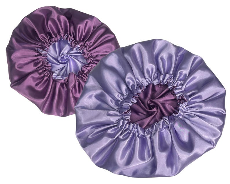 Op de afbeelding: Twee satijnen slaapmutsen, &eacute;&eacute;n paars en &eacute;&eacute;n lavendel, met een contrasterende voering. De slaapmutsen zijn ontworpen om het haar te beschermen tijdens het slapen.
