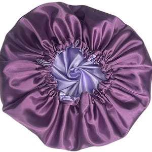 Op de afbeelding: Paarse satijnen slaapmuts met een lichtpaarse voering. De slaapmuts is bovenaan gerimpeld en heeft een gladde, zijdeachtige textuur.