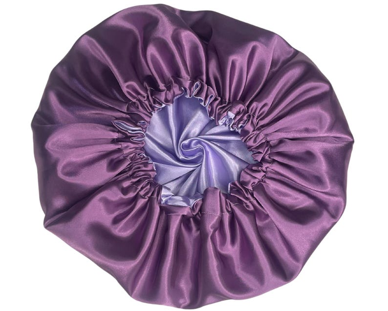 Op de afbeelding: Paarse satijnen slaapmuts met een lichtpaarse voering. De slaapmuts is bovenaan gerimpeld en heeft een gladde, zijdeachtige textuur.