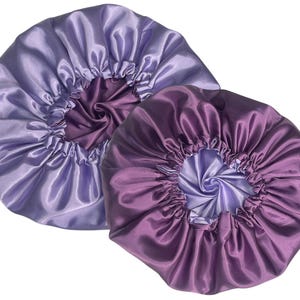 Op de afbeelding: Twee satijnen haarbonnets, een in een lichtpaarse tint en de andere in een donkerpaarse tint. Beide bonnets zijn gemaakt van zachte, zijdeachtige stof en hebben een gerimpeld ontwerp.
