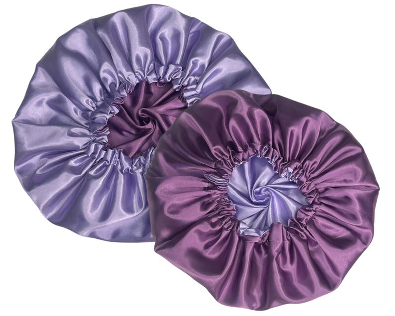 Op de afbeelding: Twee satijnen haarbonnets, een in een lichtpaarse tint en de andere in een donkerpaarse tint. Beide bonnets zijn gemaakt van zachte, zijdeachtige stof en hebben een gerimpeld ontwerp.