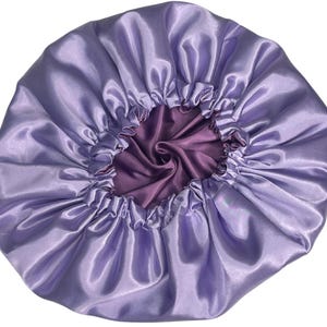 Op de afbeelding: Een lavendel satijnen muts met een paarse satijnen voering. De muts is bovenaan gerimpeld en heeft een gladde, zijdeachtige textuur.